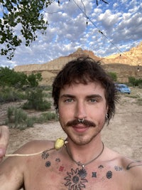 a man with tattoos on his chest in the desert